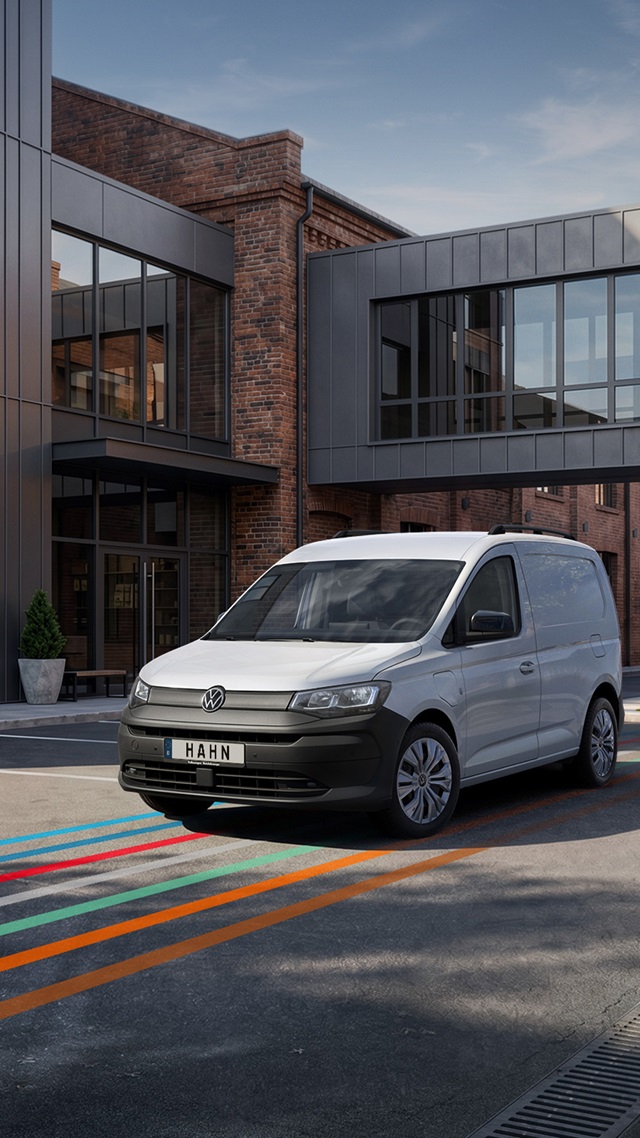 Weißer VW Caddy Cargo Kleintransporter frontal vor modernem Backstein- und Glasgebäude geparkt