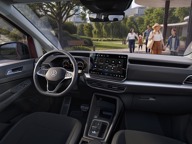Der Innenraum des VW Caddy mit Digital Cockpit, Infotainmentsystem und Personen im Hintergrund.