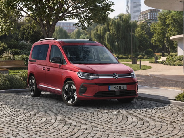 Roter VW Caddy in der Frontansicht auf einem gepflasterten Weg mit Bäumen im Hintergrund.