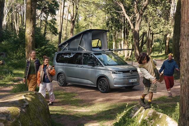 Der Volkswagen California Coast mit aufgestelltem Dach im Wald. Eine Familie ist zu sehen. 