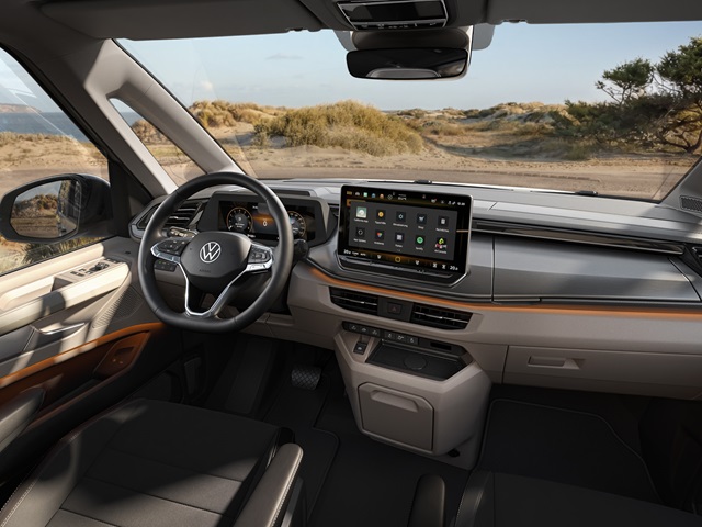 Innenraum eines VW California mit Lenkrad, digitalem Cockpit und großem mittig platziertem Touchscreen vor einer Dünenlandschaft