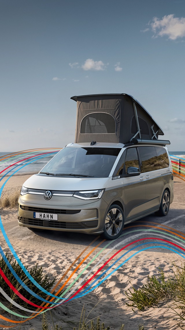 VW California Campervan in Beige-Weiß mit aufgeklapptem Dachzelt steht auf sandigem Strand mit blauem Himmel
