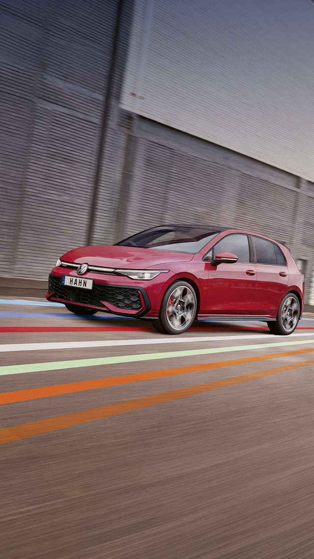 Roter VW Golf GTI fährt seitlich vor einer grauen Wand mit bunten Linien auf dem Boden