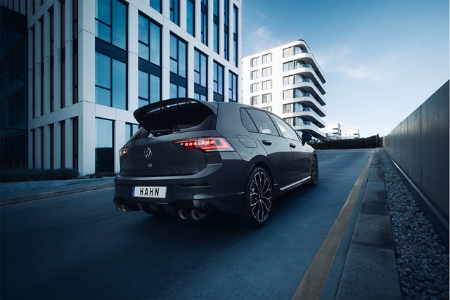 Dunkelgrauer VW Golf R-Line mit Heckspoiler und Doppelrohrauspuff fährt eine steile Straße zwischen modernen Gebäuden hinauf