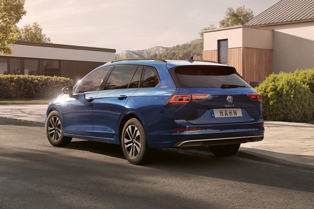 Blauer VW Golf Variant in Seitenansicht vor modernem Wohnhaus mit Bergkulisse