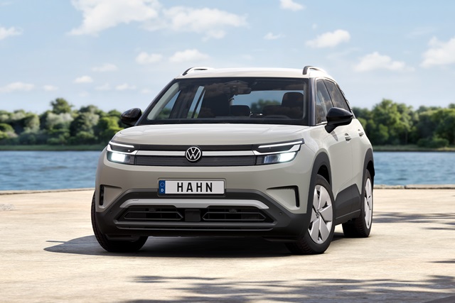 Frontansicht eines grauen VW ID. Cross mit schwarzem Kühlergrill, LED-Scheinwerfern und deutschem Kennzeichen 'HAHN' vor einem See und bewaldeter Landschaft