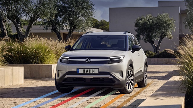 VW ID. Cross Life in Grau von vorne auf gepflastertem Platz mit Bäumen und modernem Gebäude im Hintergrund