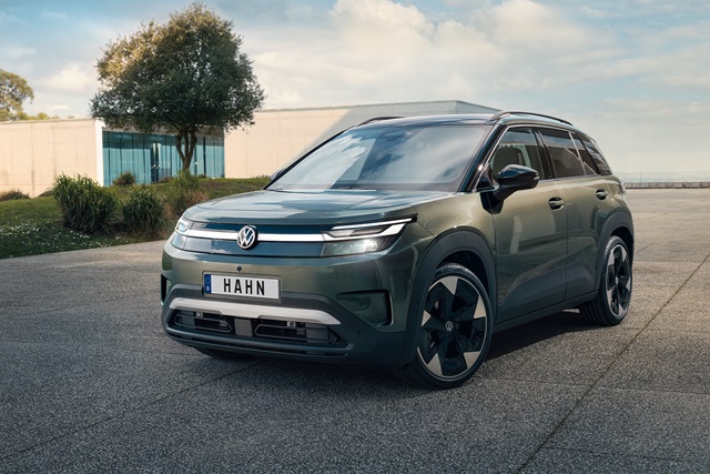 VW ID. Cross in grün mit markantem Frontdesign und schwarzem Dach steht auf gepflastertem Platz vor moderner Architektur