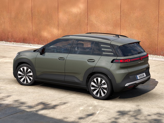Seitenansicht eines grünen VW ID. Cross mit schwarzem Dach und markanten Felgen vor einer orangefarbenen Wand