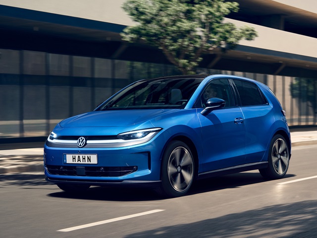 Blauer VW ID. Polo fährt auf einer Straße vor einem modernen Gebäude mit Bäumen im Hintergrund