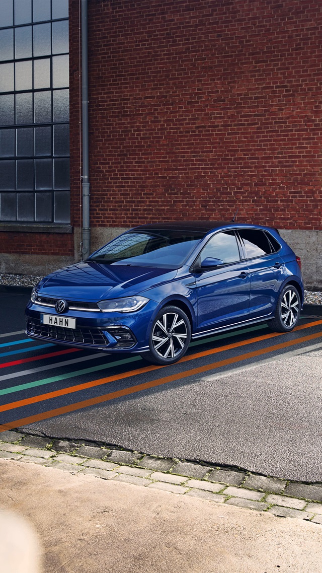 Blauer VW Polo in Seitenansicht vor roter Backsteinwand auf mehrfarbig markiertem Asphalt geparkt