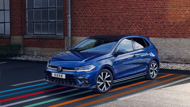 Blauer VW Polo in Seitenansicht vor roter Backsteinwand mit großen Fenstern und dem Schriftzug 'HAHN' auf dem Nummernschild