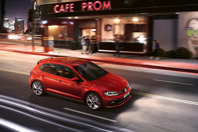 Roter VW Polo GTI fährt nachts auf einer Stadtstraße vor einem Café mit beleuchtetem Schriftzug
