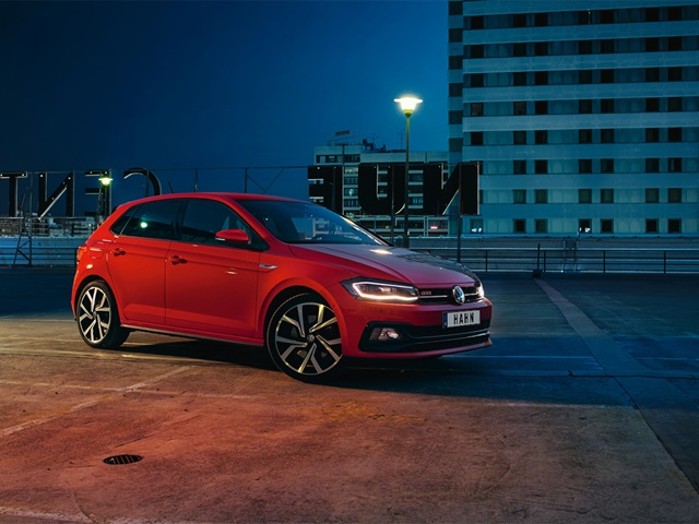 Roter VW Polo GTI in Seitenansicht auf urbanem Parkplatz bei Nacht mit beleuchtetem Hochhaus im Hintergrund