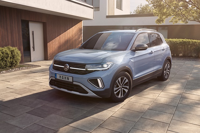 VW T-Cross in Energie Blau aus schräger Frontansicht auf einer gepflasterten Einfahrt vor einem modernen Gebäude.