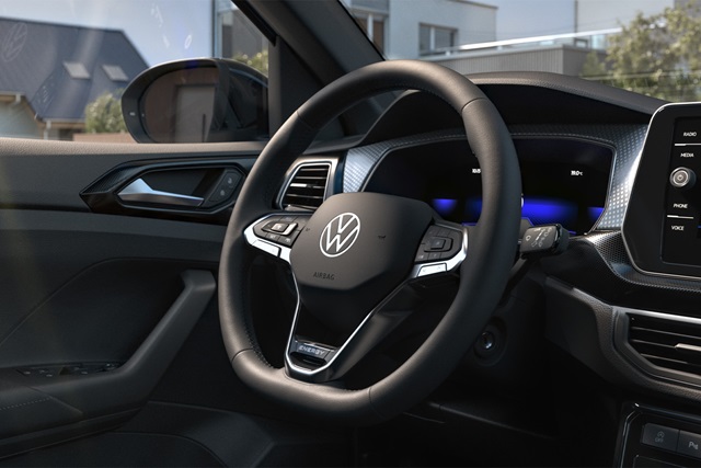 Lenkrad mit VW-Logo und Multifunktionstasten im Innenraum eines VW T-Cross vor digitalem Cockpit.