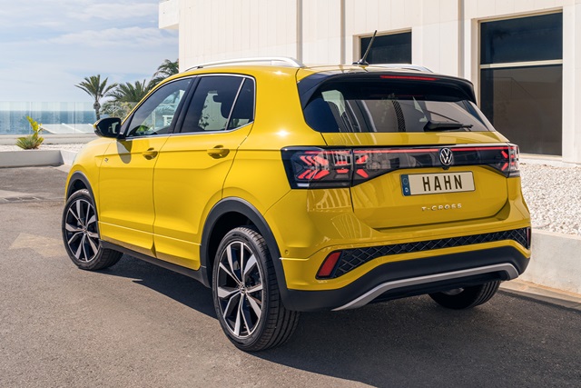 Gelber VW T-Cross R-Line aus der Rückansicht mit markanten Rückleuchten und Hahn-Kennzeichen vor einem modernen Gebäude