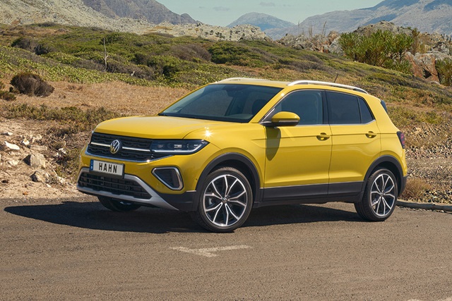 VW T-Cross Style in Gelb aus seitlicher Perspektive auf einer Straße vor hügeliger Landschaft