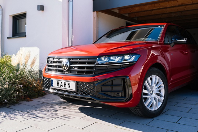 Nahaufnahme eines roten VW Touareg R-Line mit sichtbarem Kühlergrill, Scheinwerfern und silbernen Felgen vor einer Garage