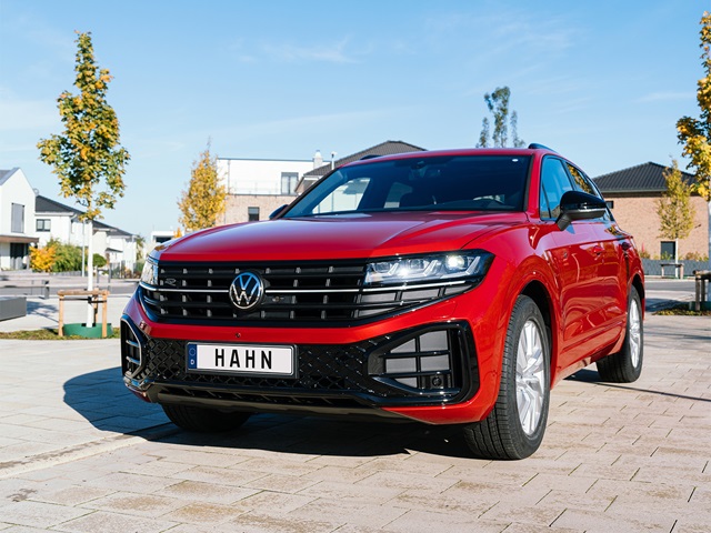 Roter VW Touareg R-Line von vorne auf gepflastertem Platz mit Hausfassaden und Bäumen im Hintergrund