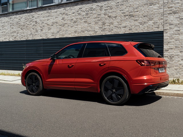 Roter VW Touareg R-Line SUV in Seitenansicht vor moderner Steinwand geparkt