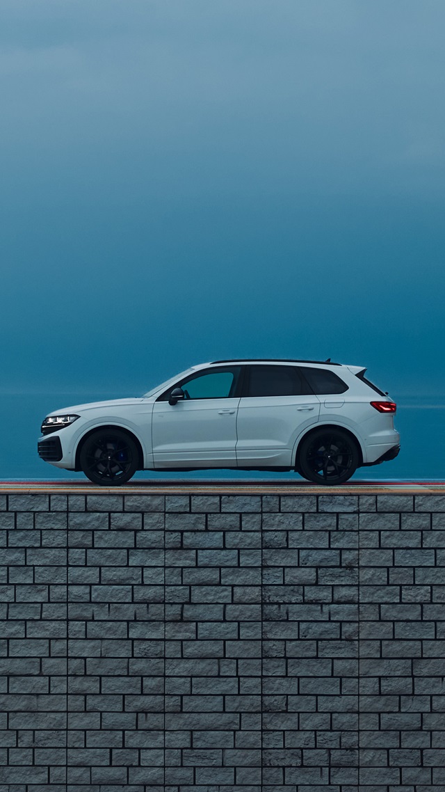 Weiße Seitenansicht eines SUV mit schwarzem Dach und schwarzen Felgen vor blauem Himmel und grauer Mauer