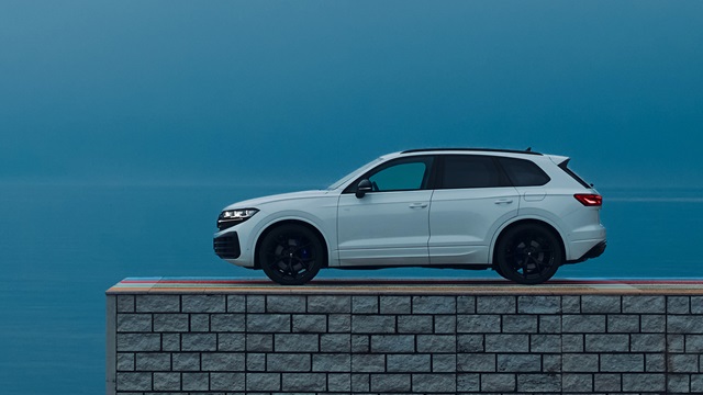 Weiße Seitenansicht eines VW Touareg R mit schwarzen Felgen auf einer Steinmauer vor blauem Himmel