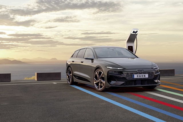 Audi A6 e-tron vor einer Ladestation bei Sonnenuntergang.