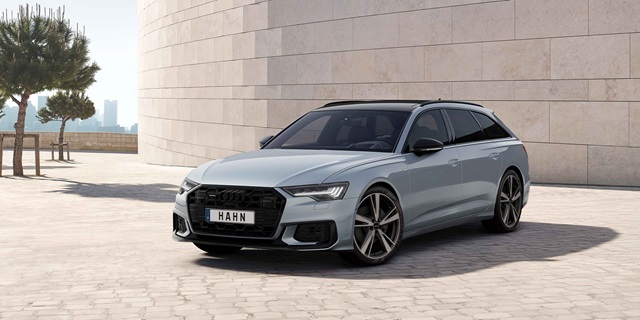 Audi Gebrauchtwagen :plus Wochen – Ein silberner Audi A6 Avant vor einer beigen Mauer.