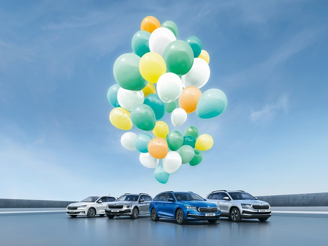 Eine Gruppe von Škoda Modellen unter bunten Luftballons vor blauem Himmel.