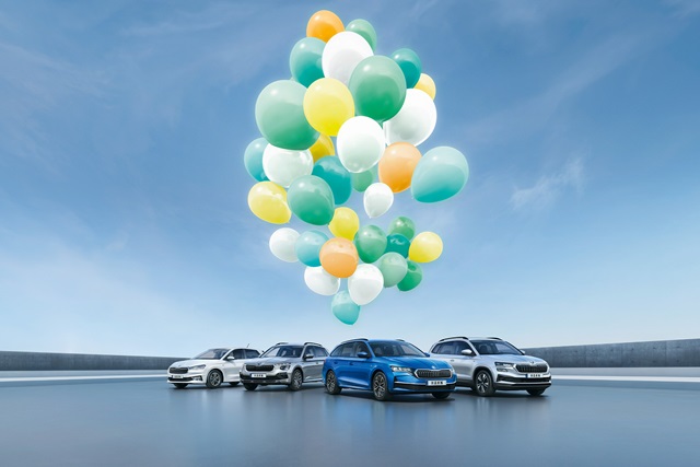 Eine Gruppe von Škoda Modellen unter bunten Luftballons vor blauem Himmel.