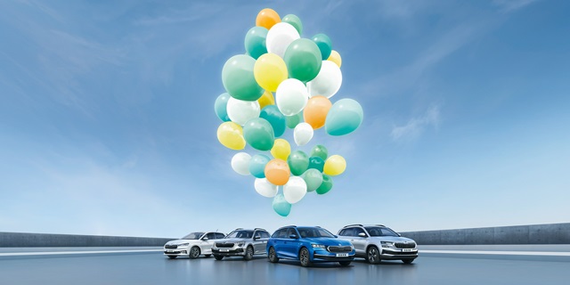 Eine Gruppe von Škoda Modellen unter bunten Luftballons vor blauem Himmel.