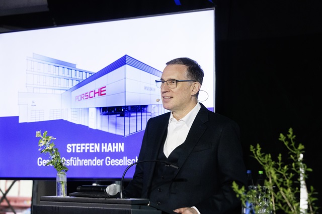 Steffen Hahn (Geschäftsführender Gesellschafter Hahn Gruppe) steht an einem Rednerpult vor einem Bildschirm mit einem Bild eines Gebäudes mit dem Schriftzug 'PORSCHE'