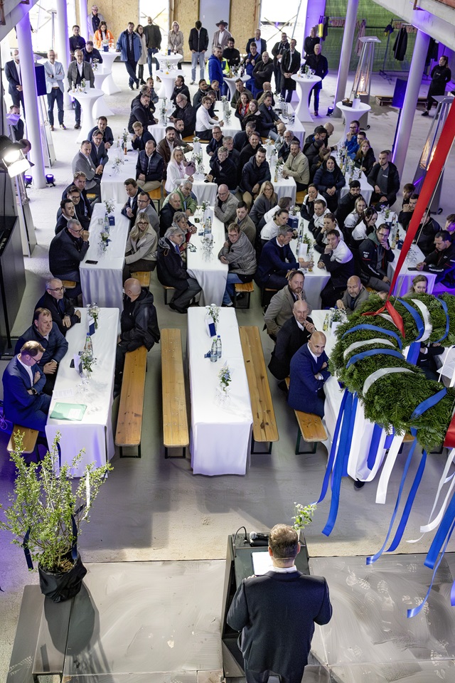Die Gäste des Richtfests sitzen an langen Tischen mit weißen Tischdecken in einer großen Halle